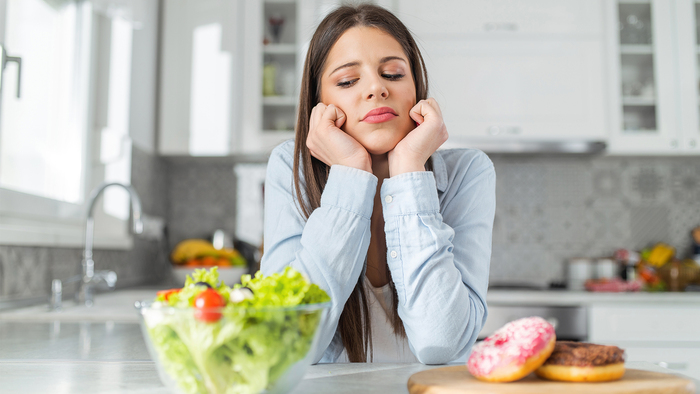 Woman choosing between doughnuts and salad